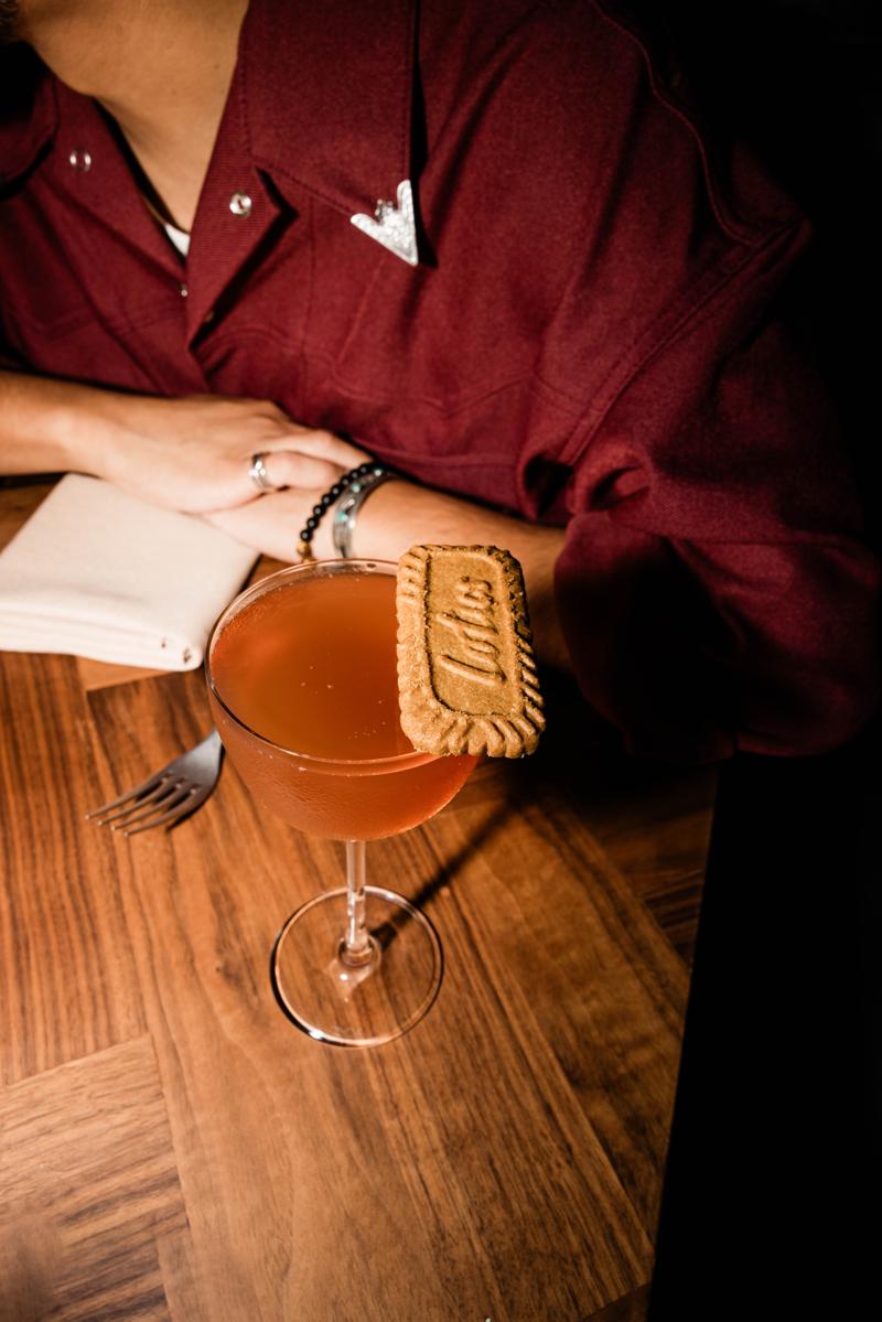 A cocktail with a cookie garnish on a walnut table