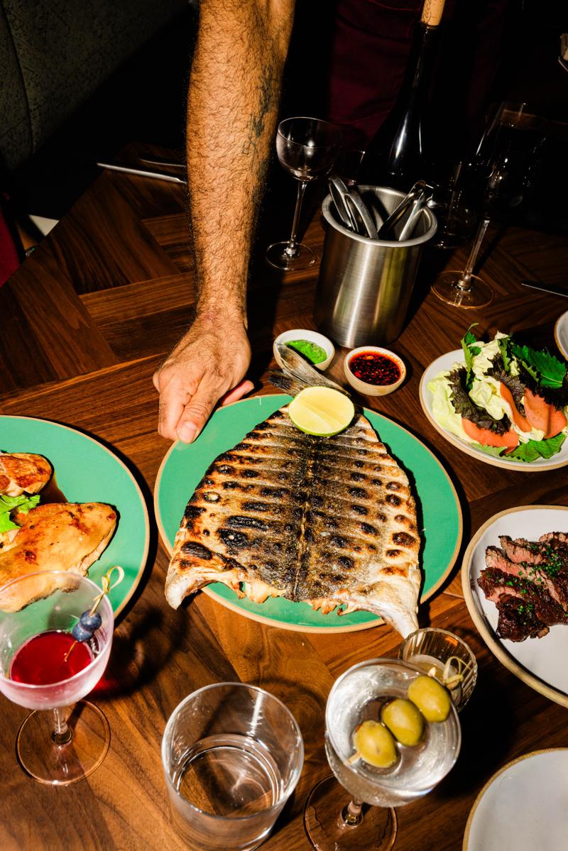 The whole branzino being set down at a full table