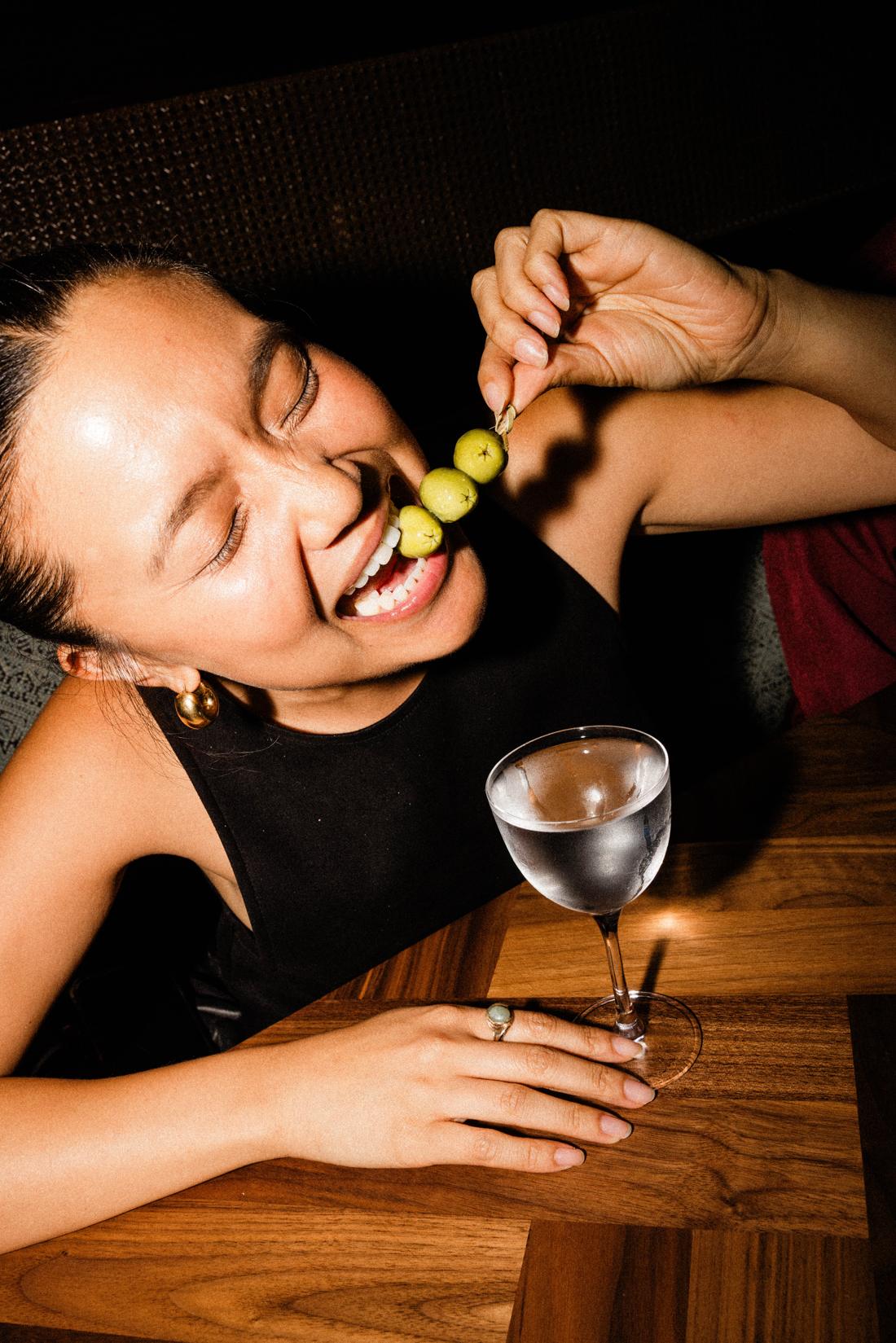 A guest laughing as she bites an olive from her martini skewer